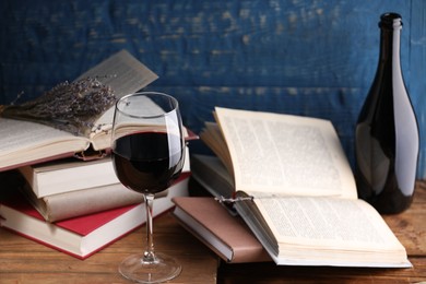 Photo of Red wine in glass, bottle, lavender flowers and books on wooden table against blue background, closeup