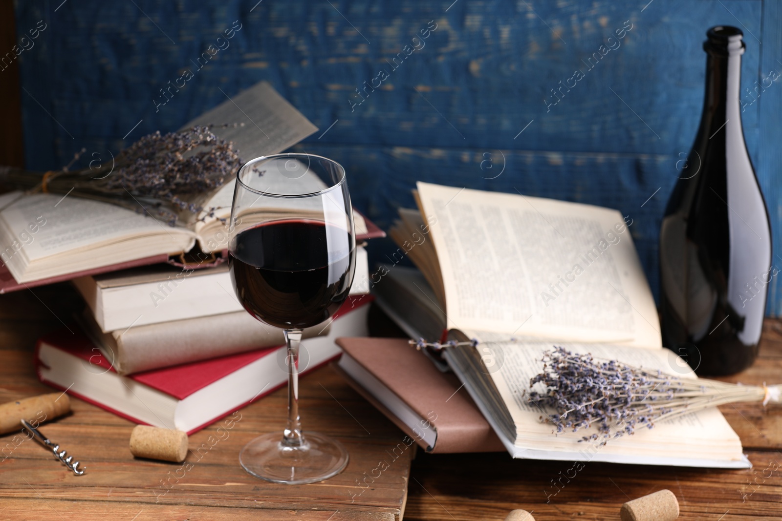 Red wine in glass, bottle, lavender flowers and books on wooden table against blue background, closeup Photo of Red wine in glass, bottle, lavender flowers and books on wooden table against blue background, closeup
