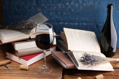 Photo of Red wine in glass, bottle, lavender flowers and books on wooden table against blue background, closeup
