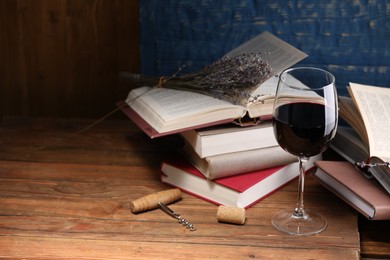 Photo of Red wine in glass, lavender flowers and books on wooden table against blue background