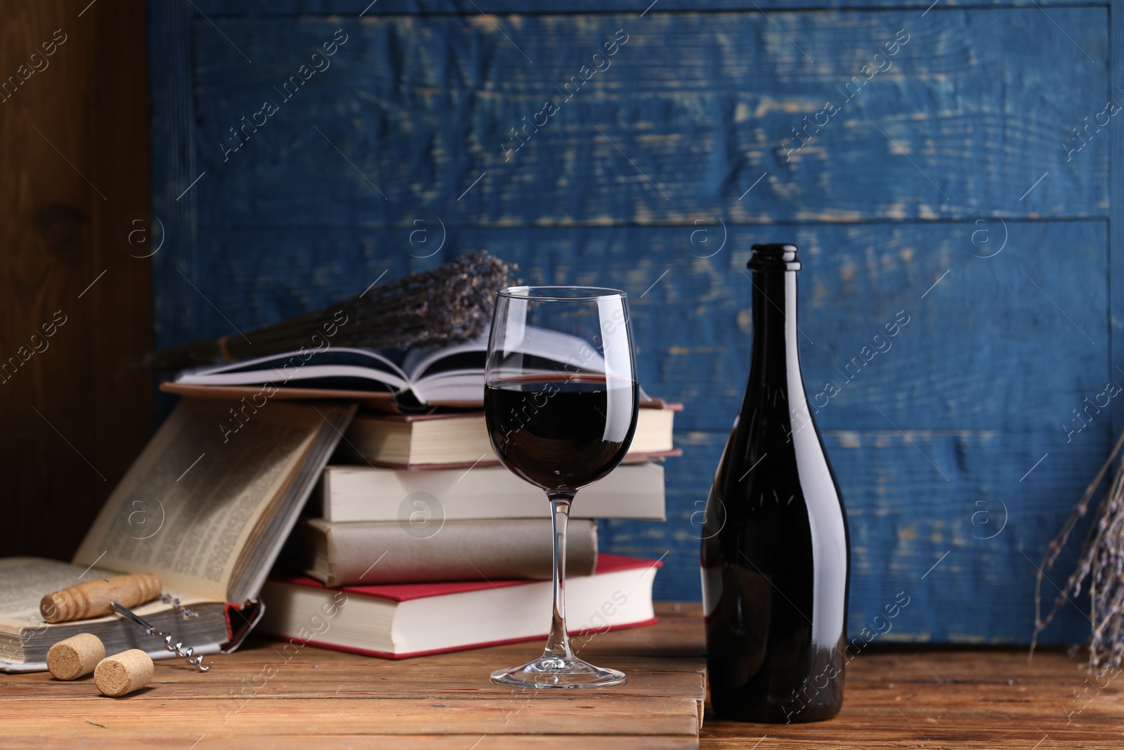 Red wine in glass, bottle, lavender flowers and books on wooden table against blue background Photo of Red wine in glass, bottle, lavender flowers and books on wooden table against blue background