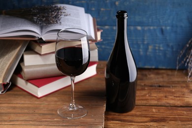 Photo of Red wine in glass, bottle, lavender flowers and books on wooden table against blue background, closeup