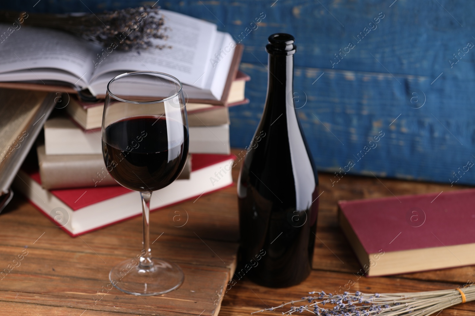 Red wine in glass, bottle, lavender flowers and books on wooden table against blue background, closeup Photo of Red wine in glass, bottle, lavender flowers and books on wooden table against blue background, closeup