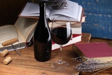 Photo of Red wine in glass, bottle, lavender flowers and books on wooden table against blue background, closeup