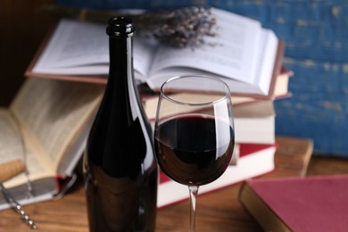 Photo of Red wine in glass, bottle and books on wooden table against blue background, closeup