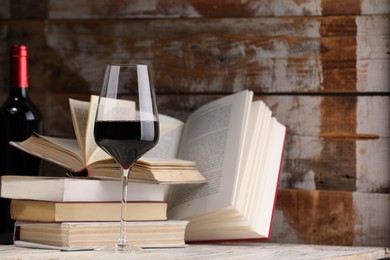 Photo of Red wine in glass, bottle and books on light table against color wooden background, closeup