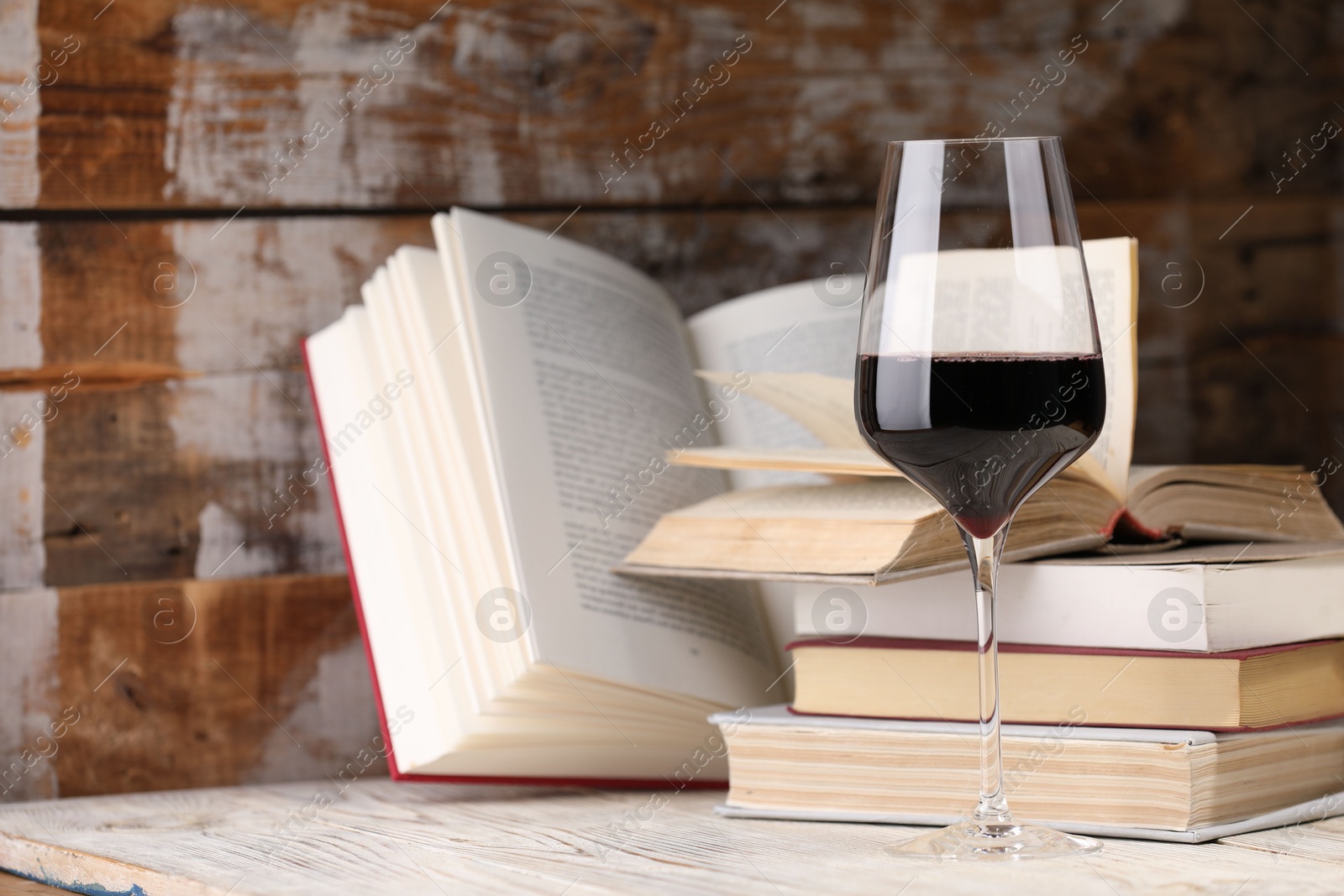 Red wine in glass and books on light table against color wooden background, closeup Photo of Red wine in glass and books on light table against color wooden background, closeup