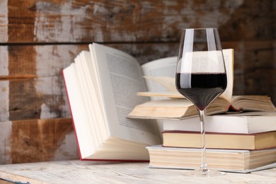 Photo of Red wine in glass and books on light table against color wooden background, closeup