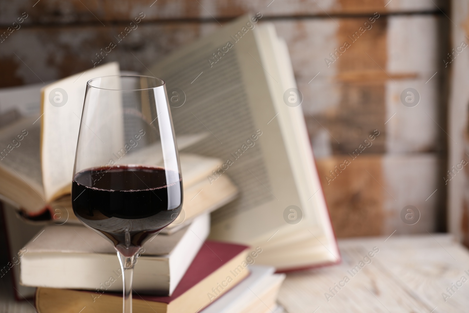 Red wine in glass and books on light table against color wooden background, closeup. Space for text Photo of Red wine in glass and books on light table against color wooden background, closeup. Space for text