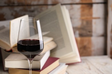 Photo of Red wine in glass and books on light table against color wooden background, closeup. Space for text