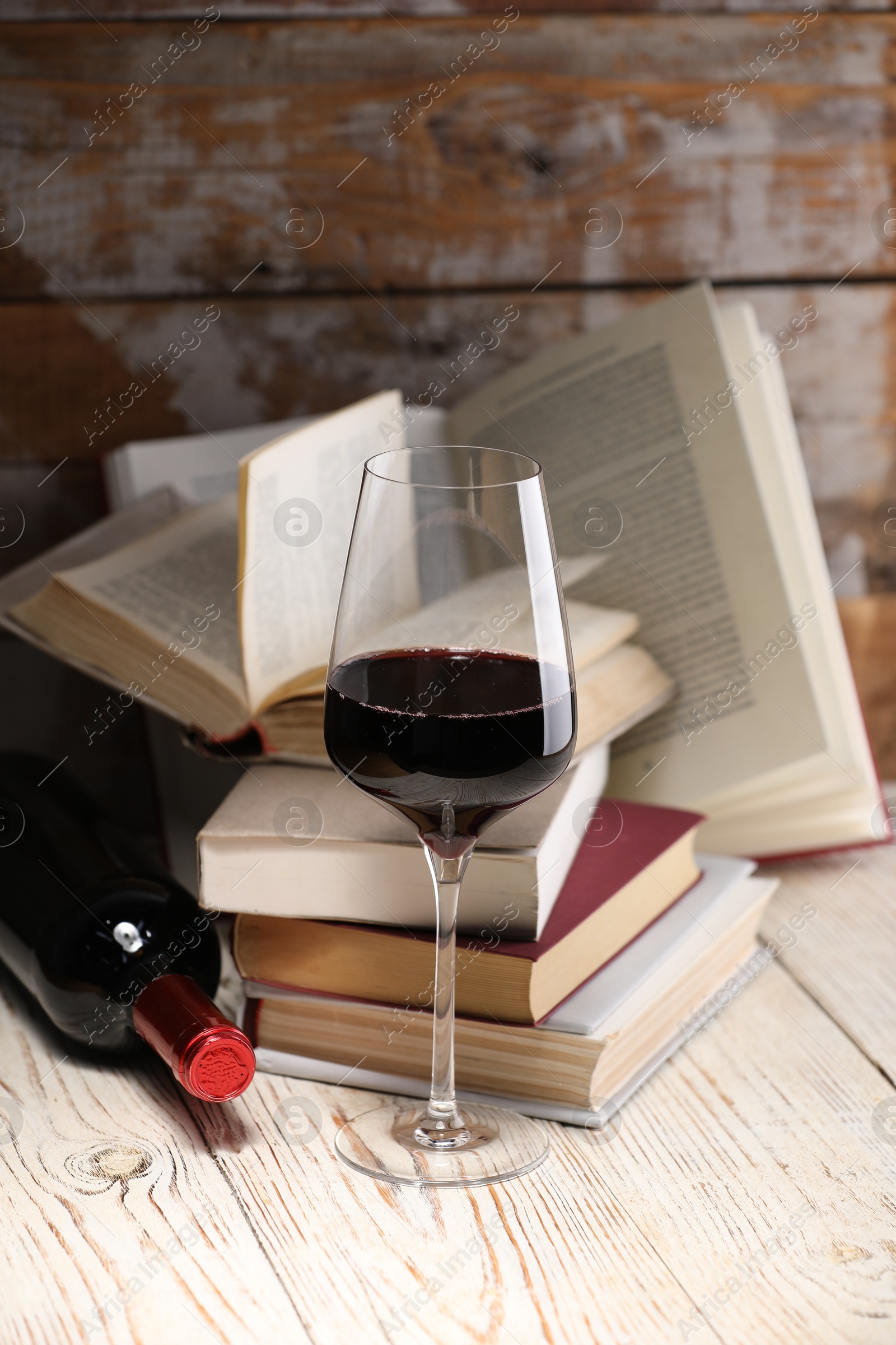 Red wine in glass, bottle and books on light table against color wooden background Photo of Red wine in glass, bottle and books on light table against color wooden background