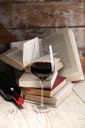 Photo of Red wine in glass, bottle and books on light table against color wooden background