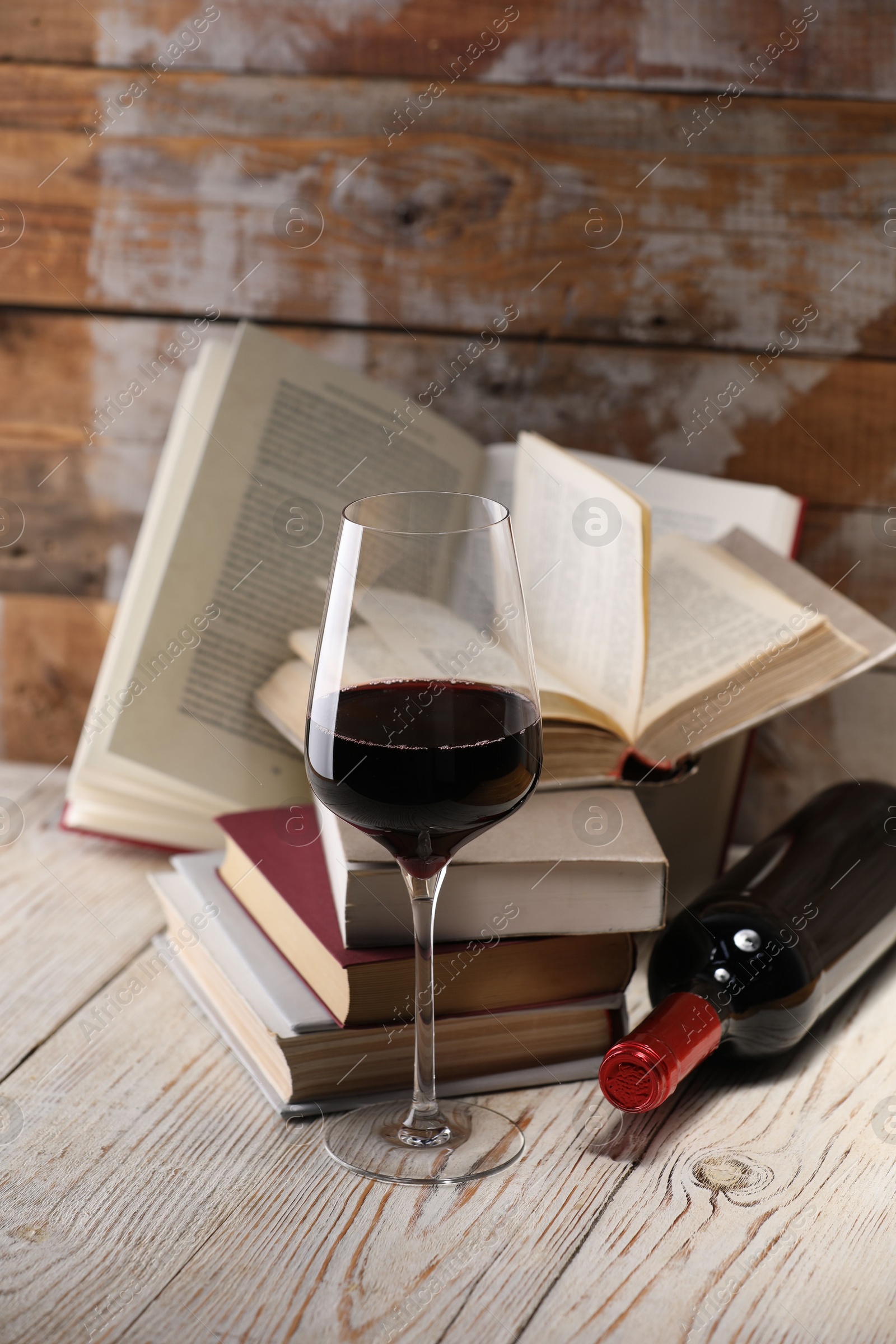 Red wine in glass, bottle and books on light table against color wooden background Photo of Red wine in glass, bottle and books on light table against color wooden background