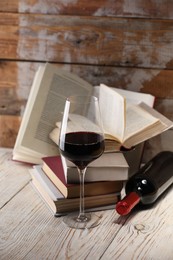 Photo of Red wine in glass, bottle and books on light table against color wooden background