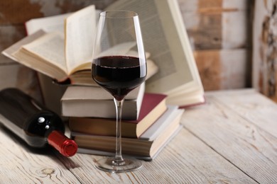 Photo of Red wine in glass, bottle and books on light table against color wooden background, closeup