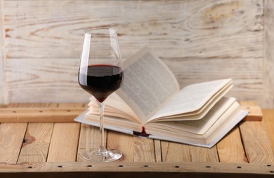 Photo of Red wine in glass and book on wooden table against light background, closeup