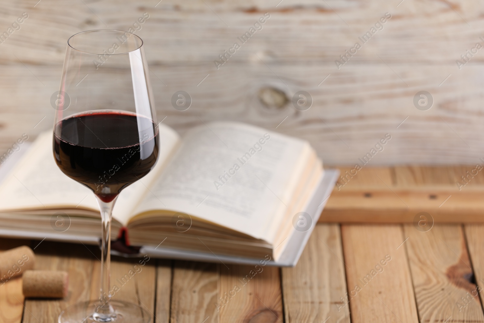 Red wine in glass and book on wooden table against light background, closeup. Space for text Photo of Red wine in glass and book on wooden table against light background, closeup. Space for text