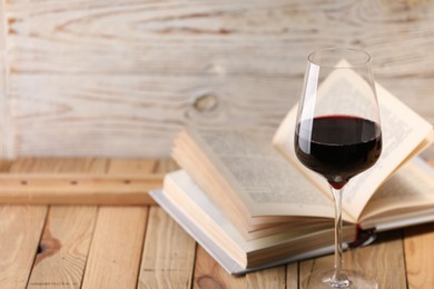 Photo of Red wine in glass and book on wooden table against light background, closeup. Space for text