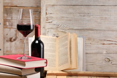 Photo of Red wine in glass, bottle and stack of books on light wooden background, closeup. Space for text