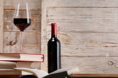 Photo of Red wine in glass, bottle and stack of books on light wooden background, closeup. Space for text