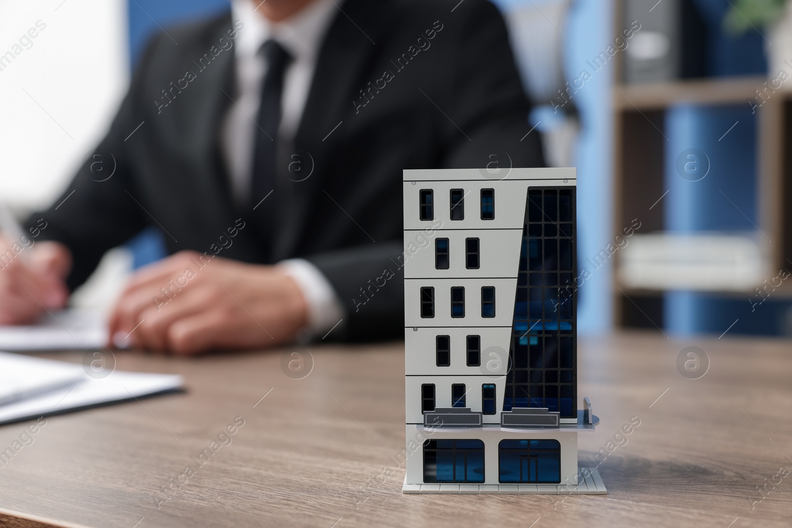 Photo of Real estate agent working at desk in office, focus on house model