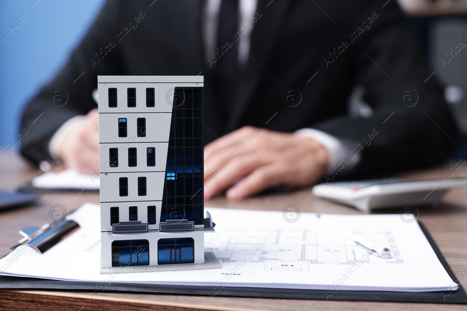 Photo of Real estate agent working at desk in office, focus on house model