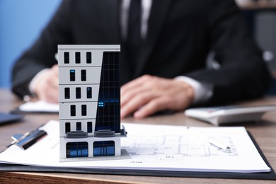 Photo of Real estate agent working at desk in office, focus on house model