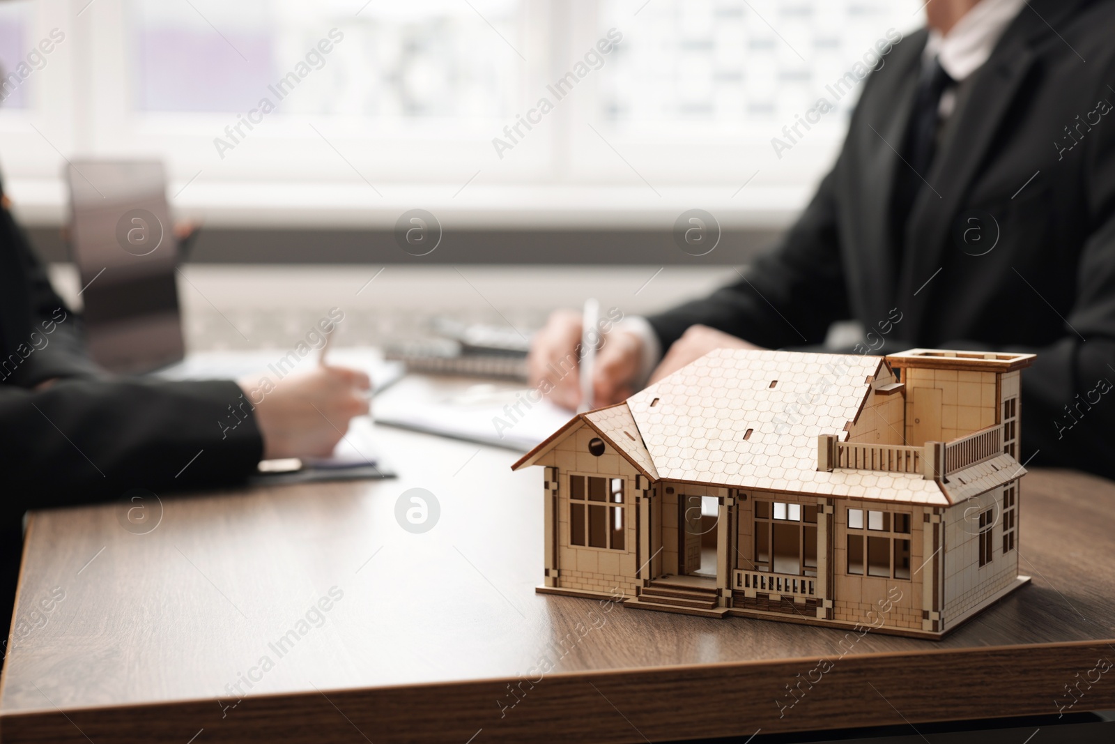 Photo of Real estate agent working with client at desk in office, focus on house model