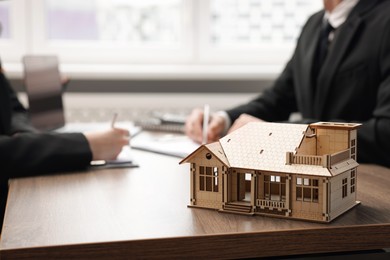 Photo of Real estate agent working with client at desk in office, focus on house model