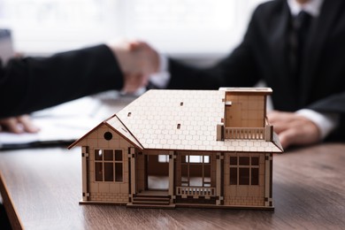 Photo of Real estate agent and client shaking hands at desk in office, focus on house model
