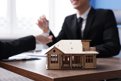 Photo of Real estate agent giving key to client at desk in office, focus on house model