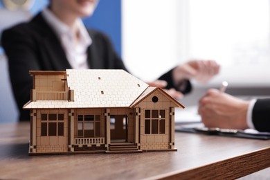Photo of Real estate agent working with client at desk in office, focus on house model