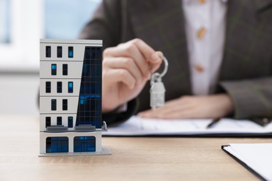 Photo of Real estate agent holding key at desk in office, focus on house model