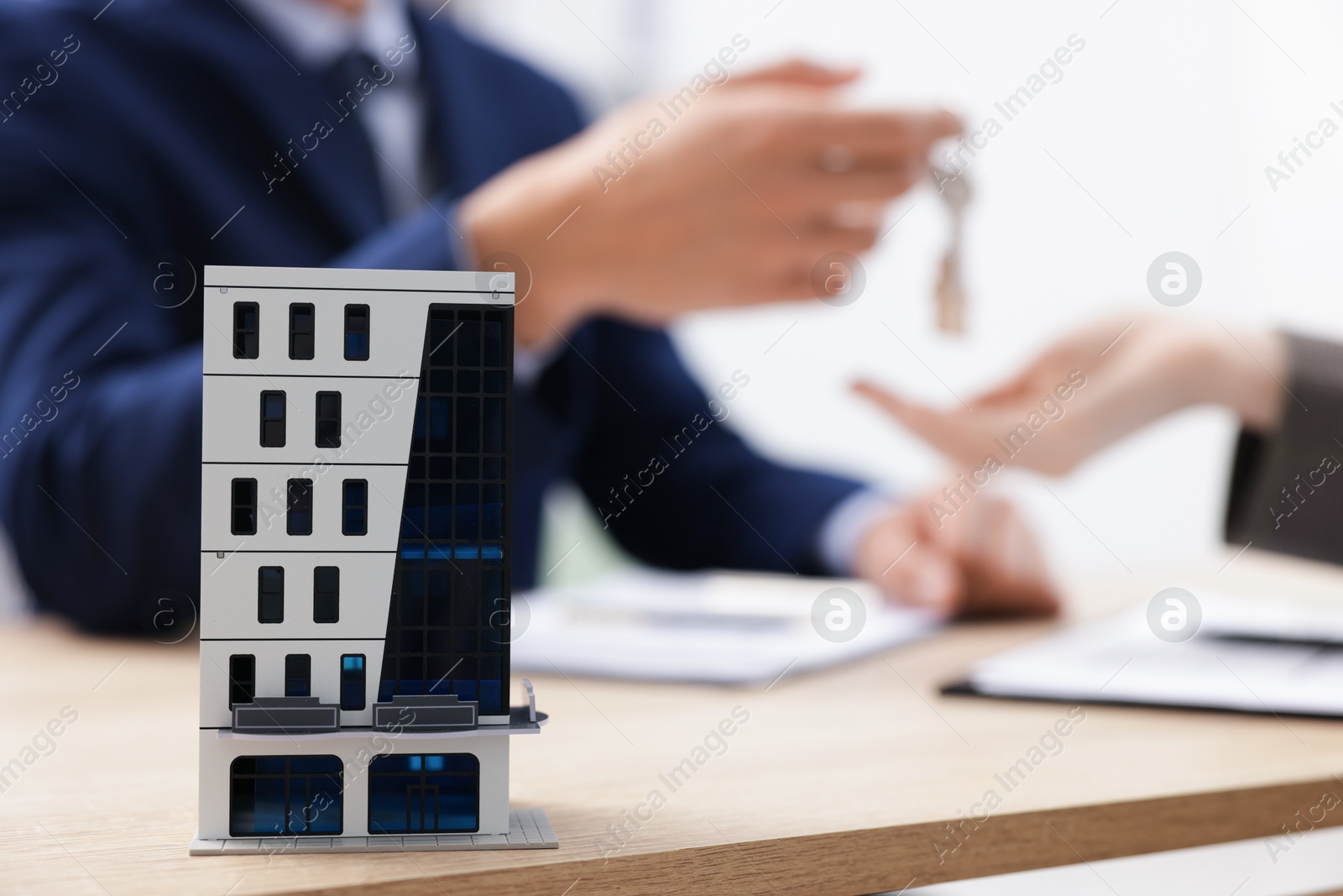Photo of Real estate agent giving key to client at desk in office, focus on house model