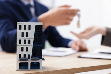 Photo of Real estate agent giving key to client at desk in office, focus on house model