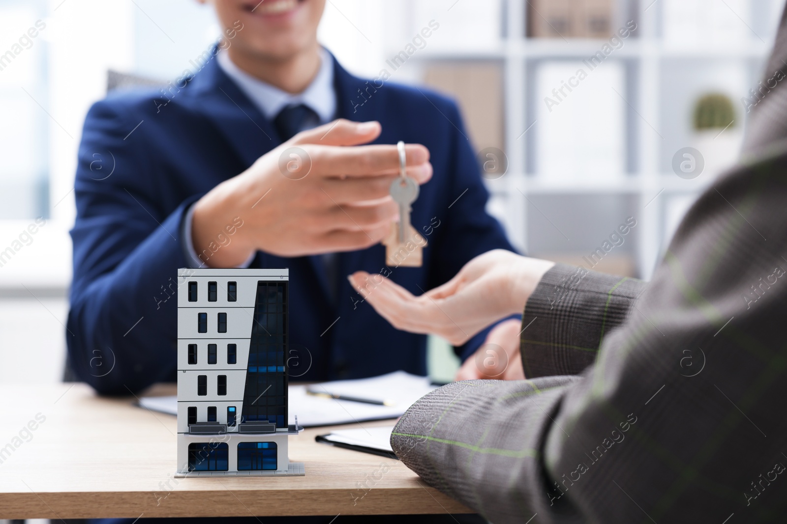 Real estate agent giving key to client at desk in office, focus on house model Photo of Real estate agent giving key to client at desk in office, focus on house model