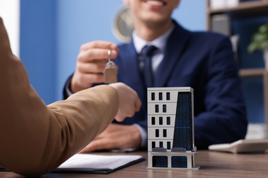 Photo of Real estate agent giving key to client at desk in office, focus on house model