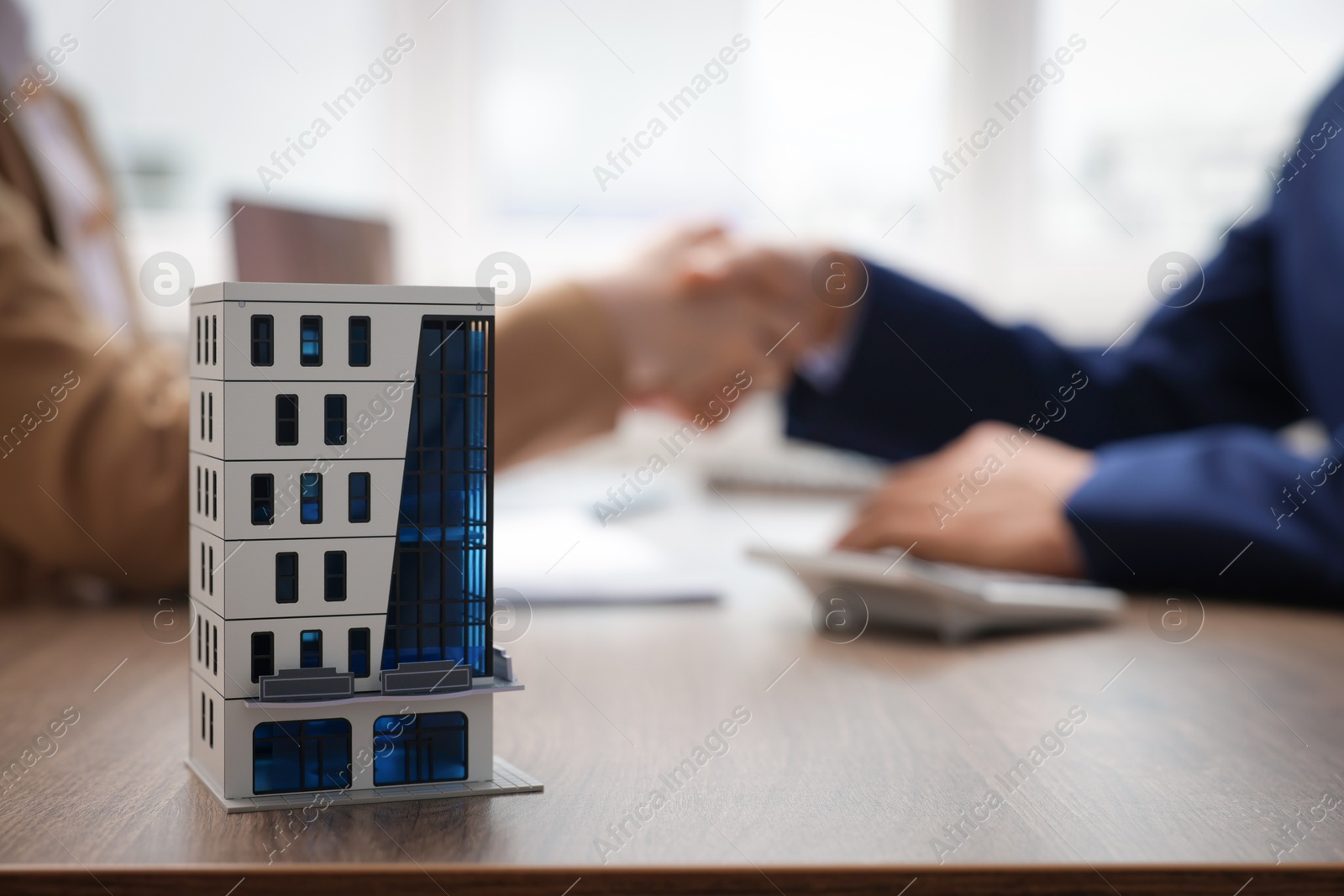 Real estate agent and client shaking hands at desk in office, focus on house model Photo of Real estate agent and client shaking hands at desk in office, focus on house model