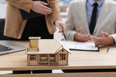 Photo of Real estate agent working with client at desk in office, focus on house model