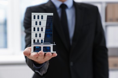 Photo of Real estate agent holding house model in office, closeup