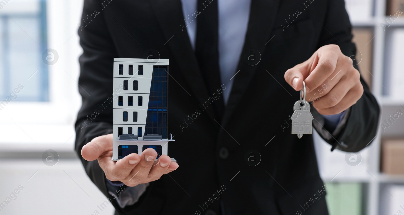 Real estate agent holding house model and key in office, closeup Photo of Real estate agent holding house model and key in office, closeup