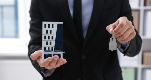 Photo of Real estate agent holding house model and key in office, closeup