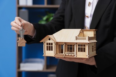 Photo of Real estate agent holding house model and key in office, closeup
