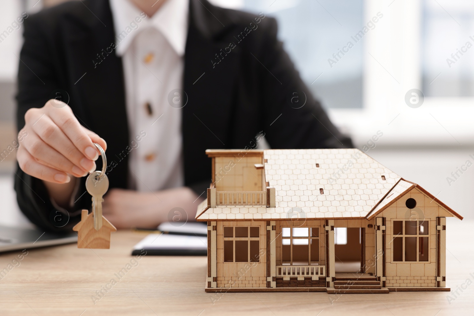 Real estate agent holding key at desk in office, focus on house model Photo of Real estate agent holding key at desk in office, focus on house model