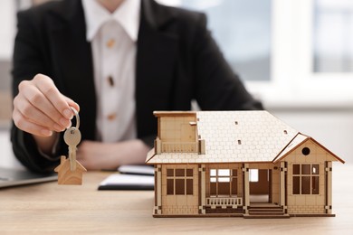 Photo of Real estate agent holding key at desk in office, focus on house model