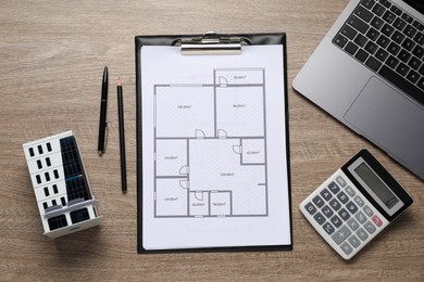Photo of Real estate. Apartment building model, floor plan, calculator and laptop on wooden table, flat lay