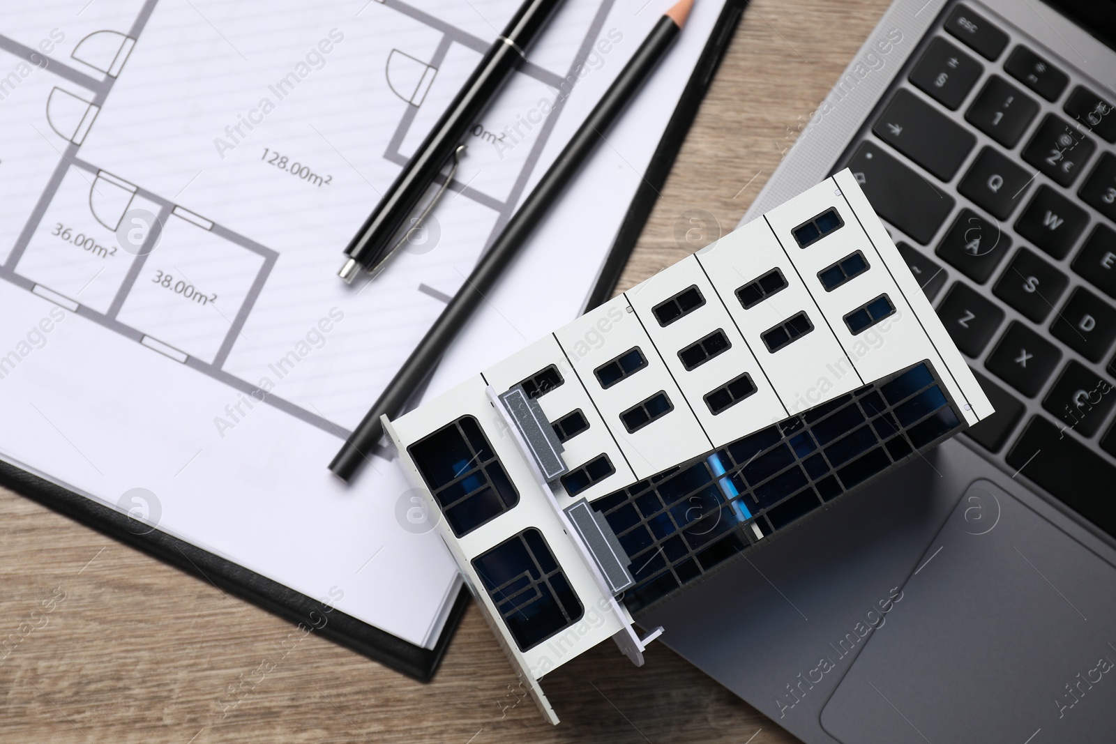 Photo of Real estate. Apartment building model, floor plan and laptop on wooden table, flat lay
