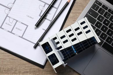 Photo of Real estate. Apartment building model, floor plan and laptop on wooden table, flat lay