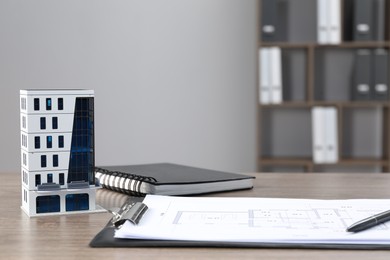 Photo of Real estate. Apartment building model, floor plan and notebook on wooden table indoors. Space for text