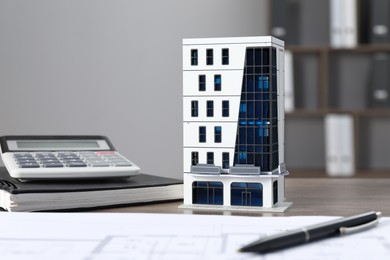 Photo of Real estate. Apartment building model, floor plan, calculator and notebook on wooden table indoors, closeup